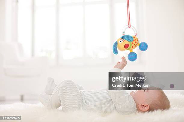 baby on rug reaching for hanging toy overhead - baby supplies stockfoto's en -beelden