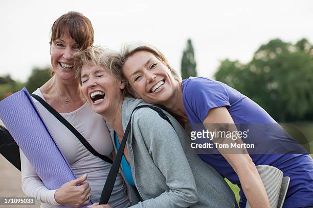 smiling women holding yoga mats - vriendin stockfoto's en -beelden