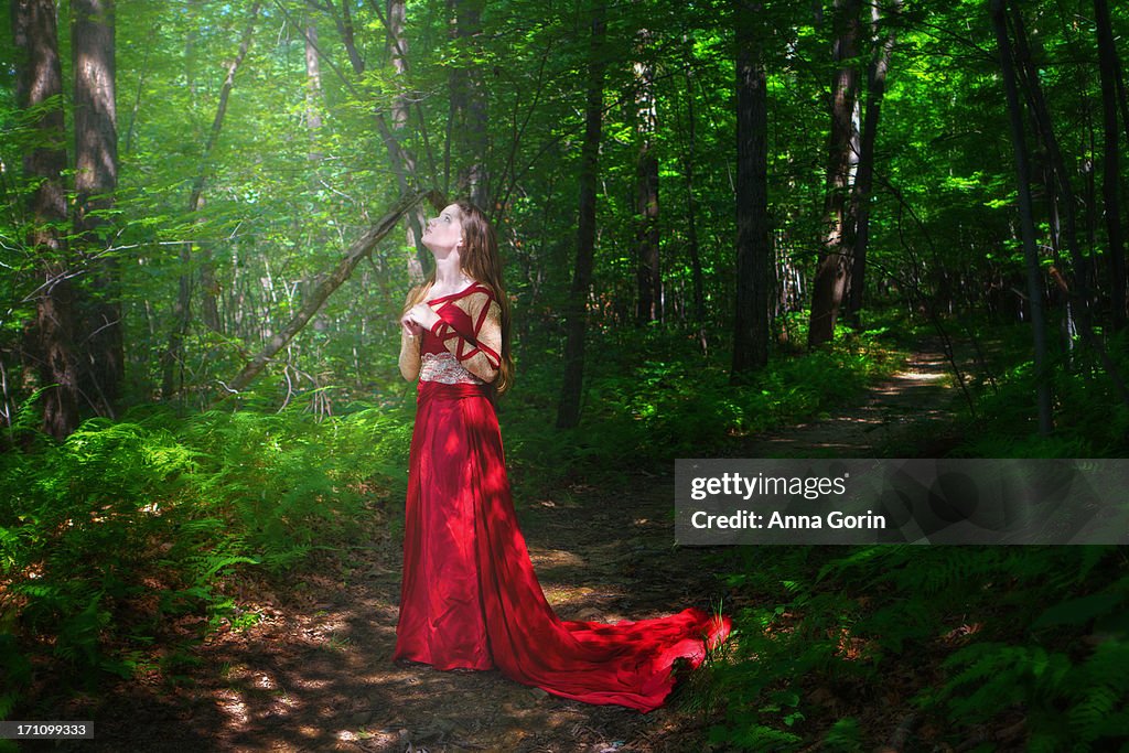 Young woman in red fantasy dress on forest path