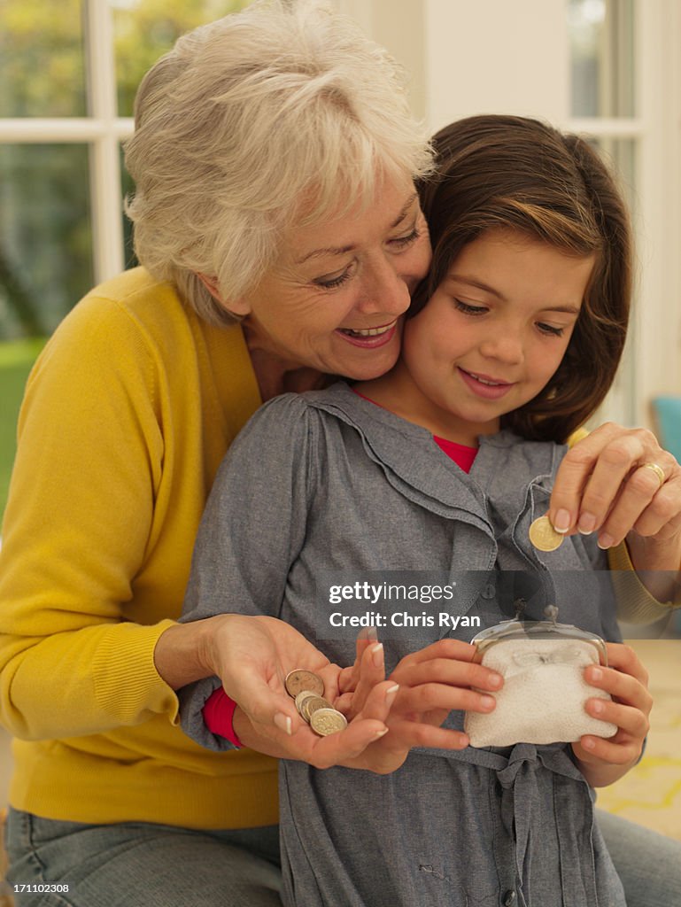 Grandmother putting coin into granddaughters piggy bank