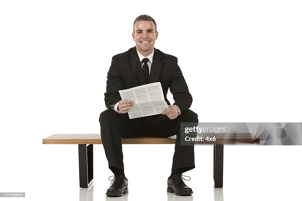 Uomo d'affari seduto sulla panchina e tenendo un giornale