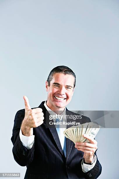 beaming businessman gives thumbs up to fistful of dollars - bundle deal stock pictures, royalty-free photos & images