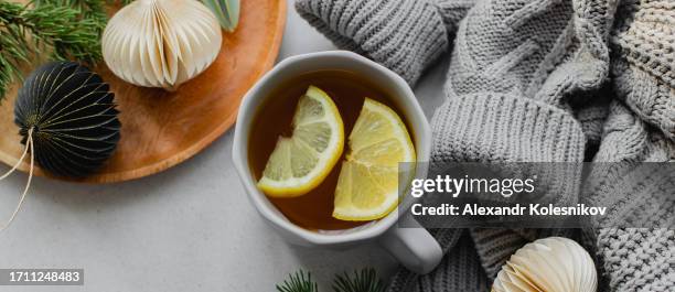 winter still life. cozy composition with cup of tea with lemon, warm sweater and festive decoration on table - cold sore stock-fotos und bilder