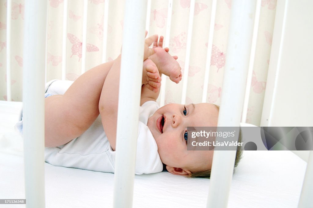 Baby holding their toes while lying in crib