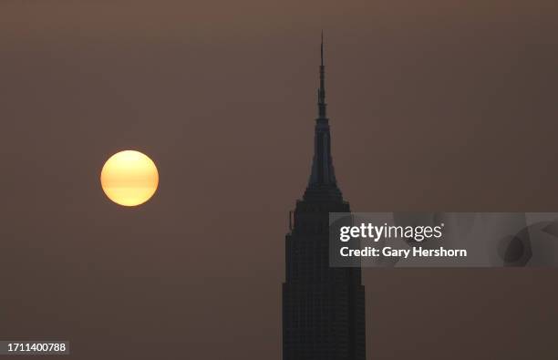 Wildfire smoke drifting back into the Northeast shrouds the sun as it rises behind the Empire State Building in New York City on October 1 as seen...