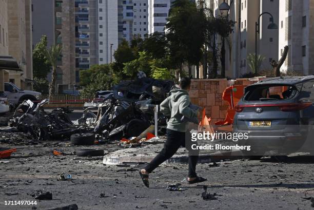 Man runs past cars destroyed in a rocket attack in Ashkelon, Israel, on Saturday, Oct. 7. 2023. Israel declared a rare state of alert for war on...