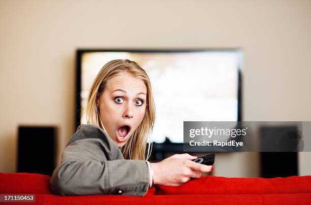 cute blonde looks round, shocked, from television in background - bad news on tv stock pictures, royalty-free photos & images