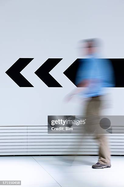 hombre caminando en la dirección opuesta de flecha - señal de salida señal de dirección fotografías e imágenes de stock