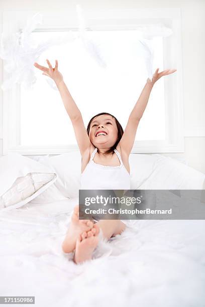 bambina felice giocare con piume nel letto - materasso foto e immagini stock