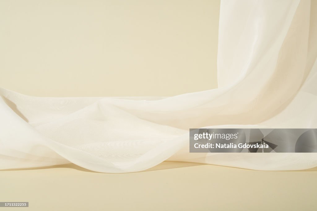 Mockup for cosmetics on light beige background, thin translucent fabric falling in waves in background. Abstract Beige Composition. Copy Space for Product Presentation.