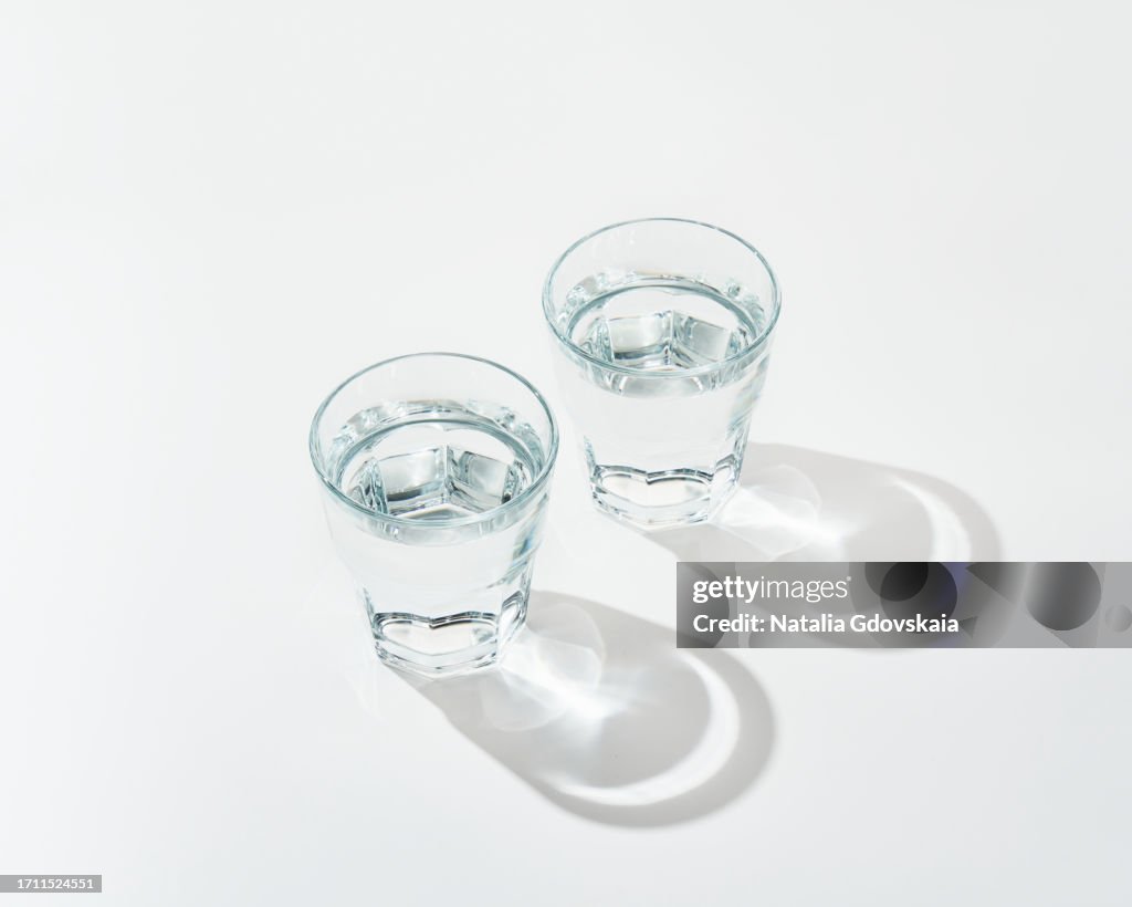 Two glass of fresh pure water on white background with sunlight deep shadow of glass. Hard sunlight.
