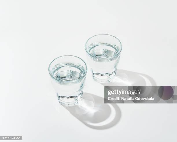 two glass of fresh pure water on white background with sunlight  deep shadow of glass. hard sunlight. - clear water stock pictures, royalty-free photos & images