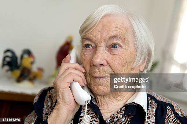 female senior is holding a phone and looks sad - landline telephone stock pictures, royalty-free photos & images