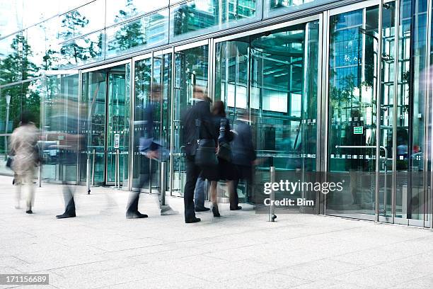 businesspeople entering through glass doors of office building, blurred motion - bustling office stock pictures, royalty-free photos & images