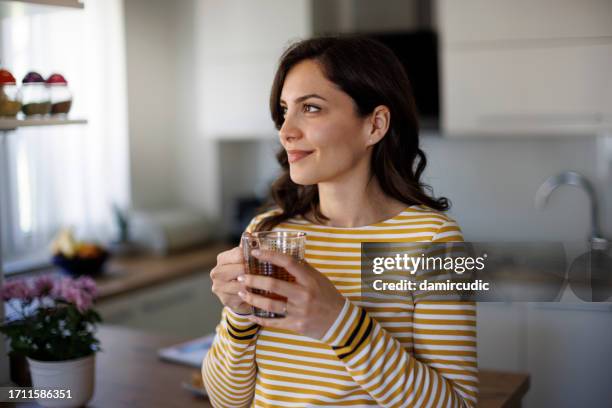 mujer joven sonriente disfrutando del té en casa - herbal tea fotografías e imágenes de stock