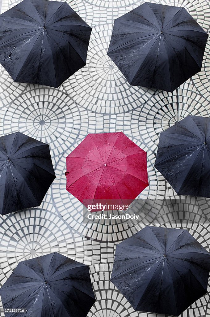 One red umbrella encircled by black umbrellas