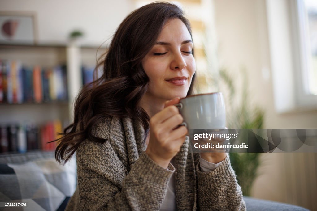 Junge lächelnde Frau genießt den Duft von frischem Kaffee zu Hause
