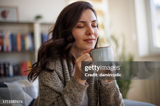 Junge lächelnde Frau genießt den Duft von frischem Kaffee zu Hause Junge lächelnde Frau genießt den Duft von frischem Kaffee zu Hause