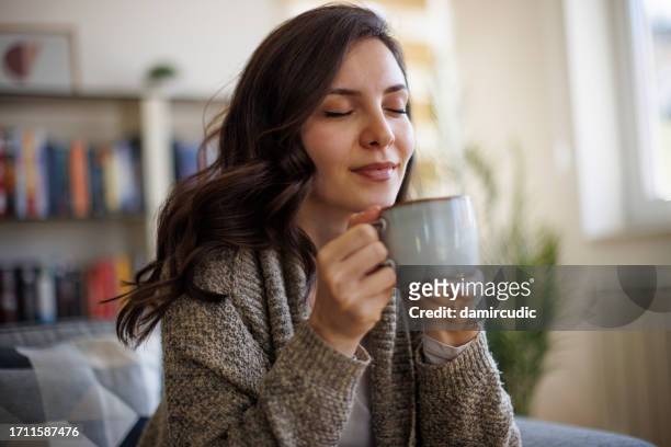 young smiling woman enjoying in smell of fresh coffee at home - drinking tea in a cup stock pictures, royalty-free photos & images