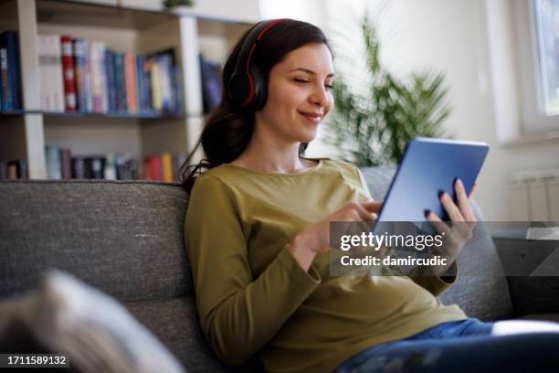 smiling relaxed woman resting on couch using digital tablet - streaming television stock pictures, royalty-free photos & images