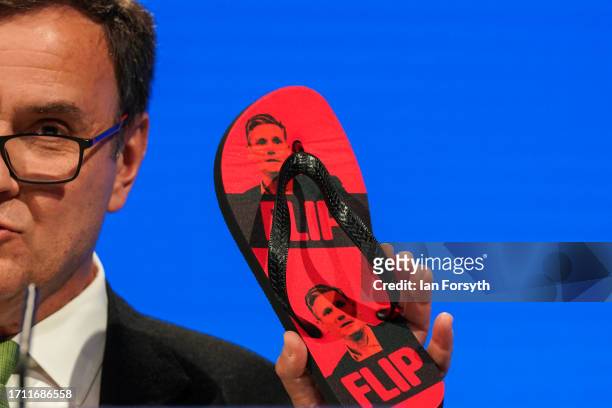 Greg Hands MP, Chairman of the Conservative Party holds up some flip-flops with the image of Labour leader Keir Starmer on them as he gives a speech...