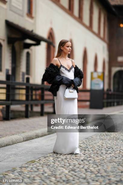 Guest wears a white strappy lingerie long dress with a black lace trim, a white bag, a fur-lined black leather jacket , outside Alberta Ferretti,...