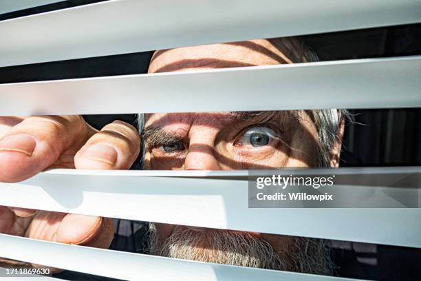 close-up senior man staring through window blinds fearfully - peeking stock pictures, royalty-free photos & images