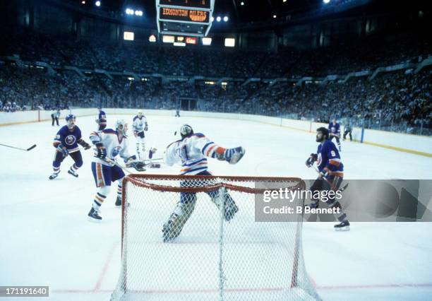 Goalie Grant Fuhr and Kevin Lowe of the Edmonton Oilers follow the puck in the air as Bryan Trottier and Clark Gillies of the New York Islanders look...