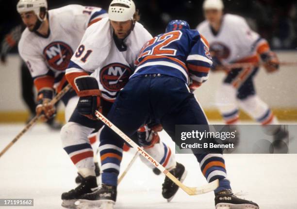 Butch Goring of the New York Islanders goes for the puck as he is checked by Charlie Huddy of the Edmonton Oilers during the 1984 Stanley Cup Finals...