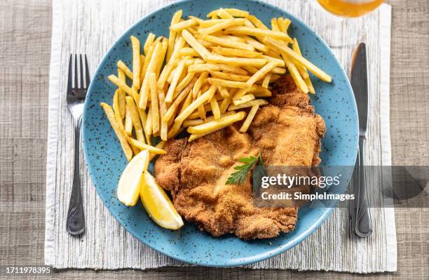 fried schnitzel with fries and lemon on a plate in a restaurant or pub. - breaded stock pictures, royalty-free photos & images