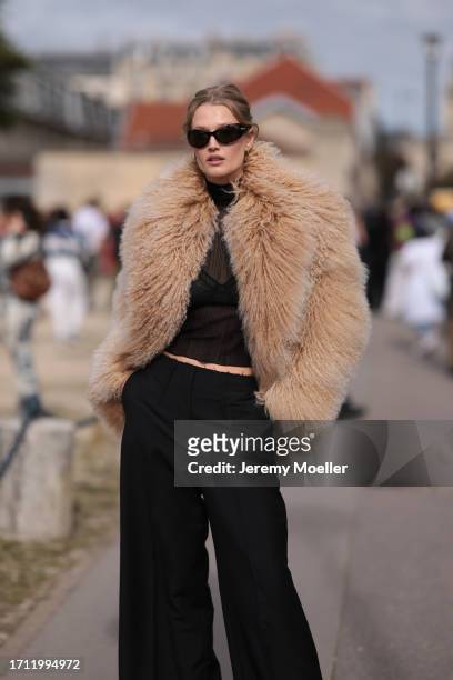 Toni Garrn is seen wearing a brown oversized fur jacket, with a black transparent top, black bralette, high-cut black pants and black sunglasses...