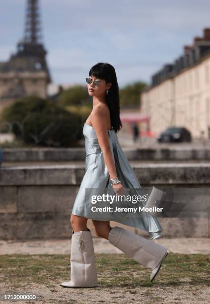 Jihoon Kim is seen wearing a light blue strapless satin dress with ruffles at the back, tall grey leather boots, a grey handbag with silver chain and...