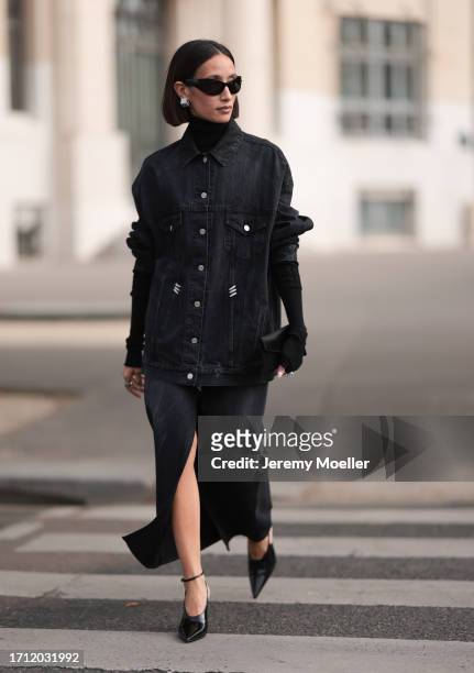 Alexandra Guerain is seen wearing a black oversized jeans jacket with silver buttons, a black turtleneck pullover under the jacket, a black midi...