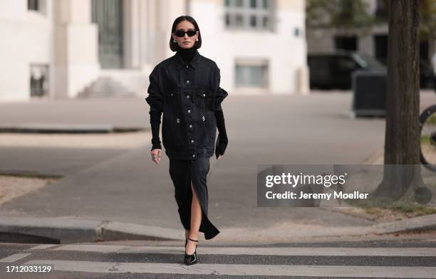 Alexandra Guerain is seen wearing a black oversized jeans jacket with silver buttons, a black turtleneck pullover under the jacket, a black midi...