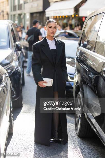 Sophia Roe wears black tailored coat, white bag, dress, white button shirt, tights outside Valentino during the Womenswear Spring/Summer 2024 as part...