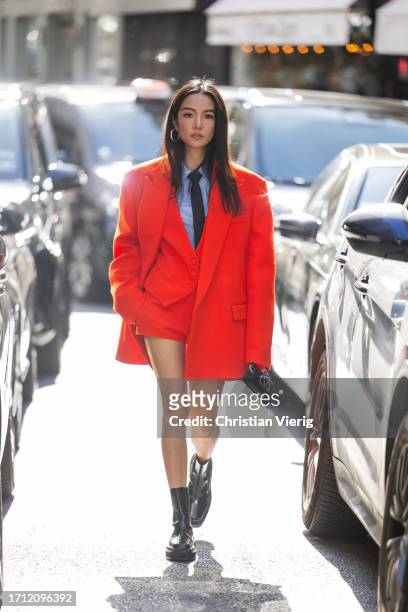 Yoyo Cao wears red oversized blazer, shorts, black tie, blue button shirt, black bag, boots outside Valentino during the Womenswear Spring/Summer...