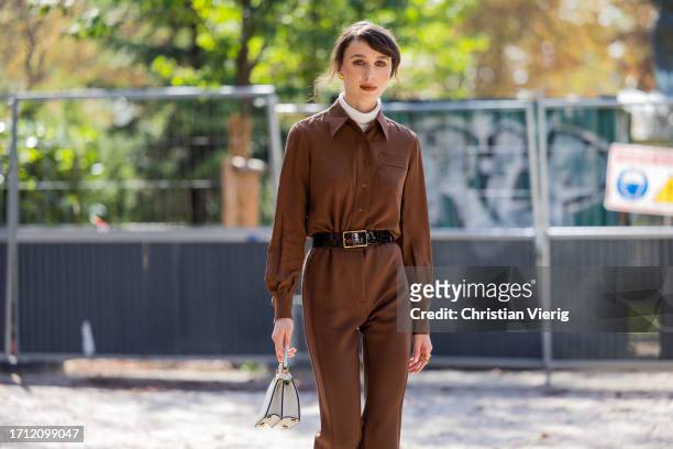 Mary Leest wears brown overall, black belt, white turtleneck, creme white bag outside Akris during the Womenswear Spring/Summer 2024 as part of Paris...