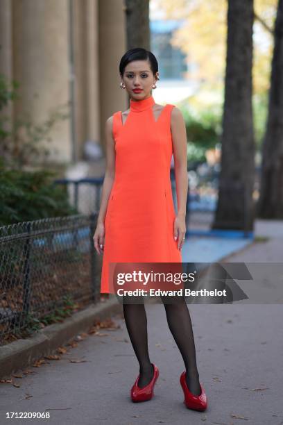 Guest wears a turtleneck neon orange dress, black tights, red shoes, earrings, outside Akris, during the Womenswear Spring/Summer 2024 as part of...