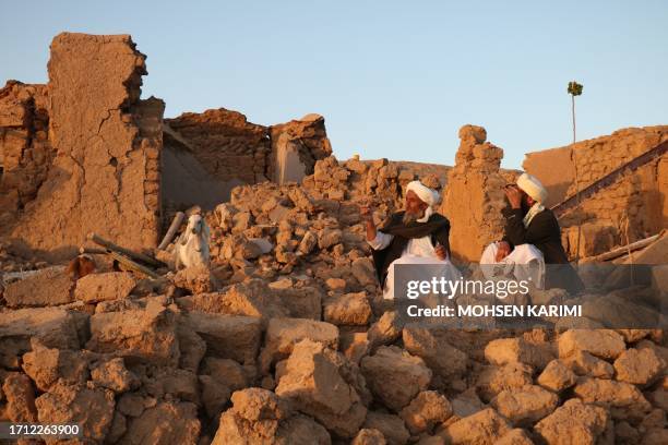 Afghan residents sit at a damaged house after earthquake in Sarbuland village of Zendeh Jan, district of Herat province, on October 7,2023