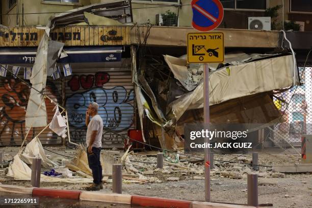 Man stands in front of a damaged shop in Tel Aviv, after it was hit by a rocket fired by Palestinian militants from the Gaza Strip on October 7,...