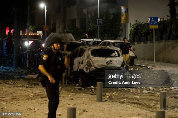 TEl AVIV, ISRAEL Police officer stand near a burned car at a scene where a rocket fired from Gaza strip hit a building on October 7, 2023 in Tel...