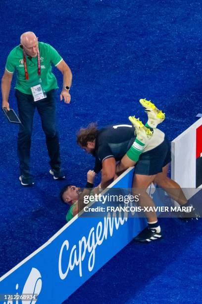 An official looks on as Scotland's loosehead prop Pierre Schoeman and Ireland's hooker Dan Sheehan tussle across an advertising hoarding during the...