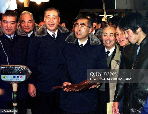 Japanese Prime Minister Keizo Obuchi holds a sea bream early 16 December 1999 during his tour to the Tsukiji Fish Market in Tokyo. Others pictured...