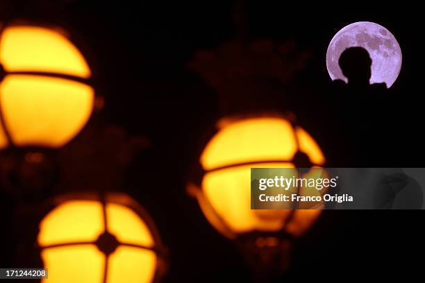 View of the full moon with a silhouette of a sculpture of the St. Peter's colonnade and framed by the 19th-century lamp posts around the obelisk of...