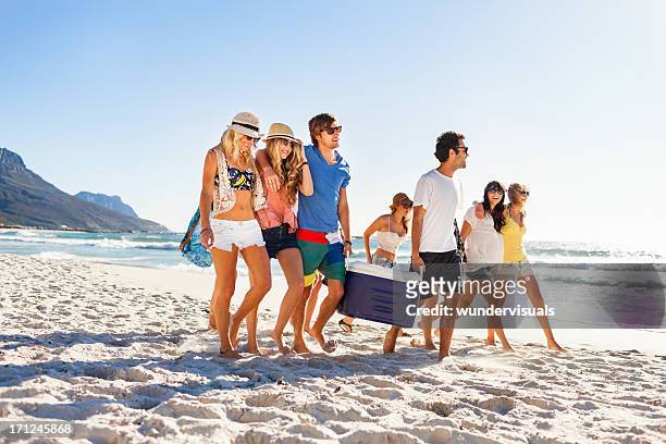 group of people carrying cooler to party on beach - beach party stockfoto's en -beelden