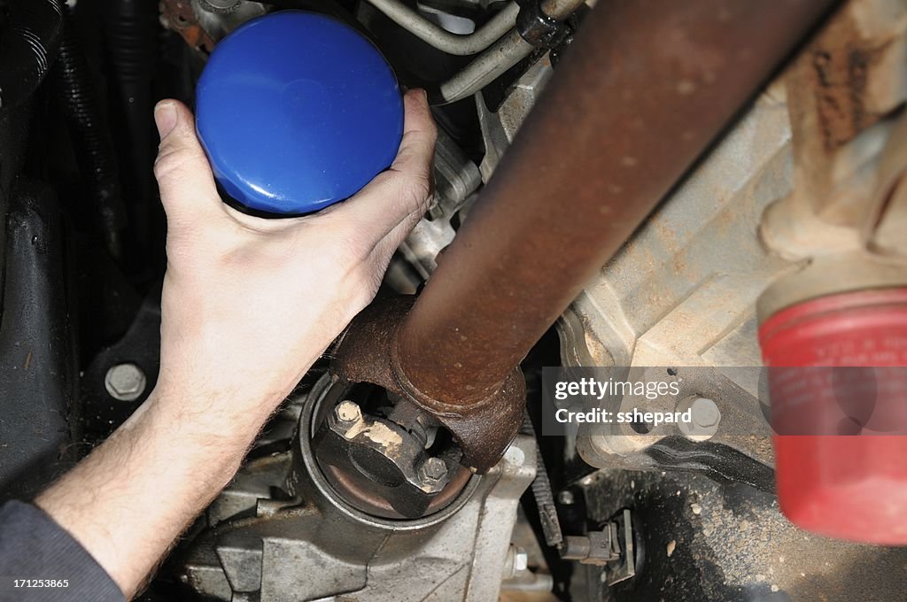 Hand grabbing oil filter under truck or car
