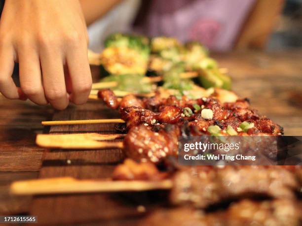 a girl's hand is picking up the freshly grilled skewers, which are placed on a wooden plate - chicken skewers stockfoto's en -beelden