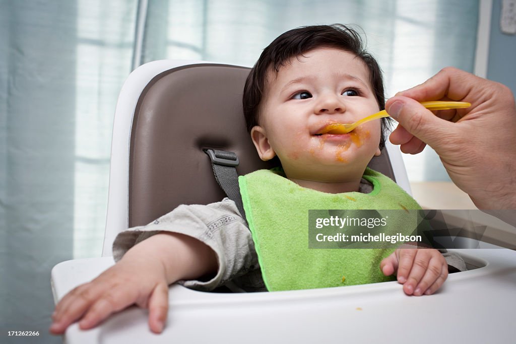 Father feeding Baby sweet potato in a high chair