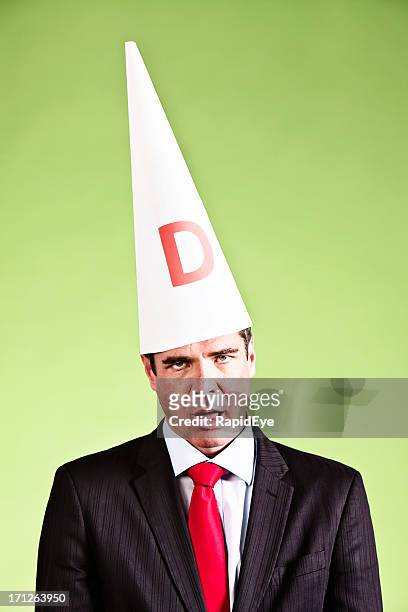 humorous study of businessman looking dumb in dunce cap - dunce cap 個照片及圖片檔