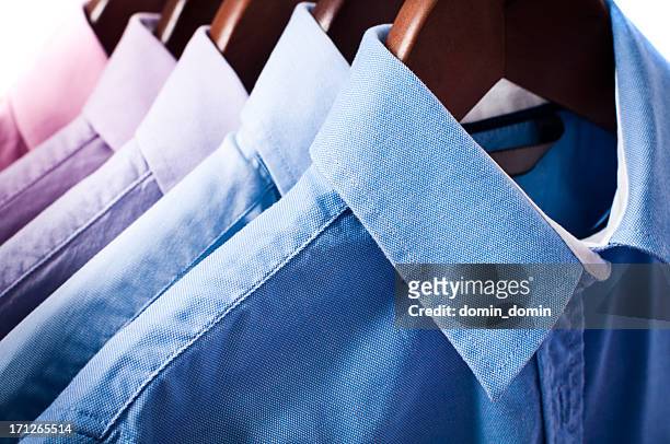 blue and pink elegant button down shirts hanging on hangers - stomerij stockfoto's en -beelden